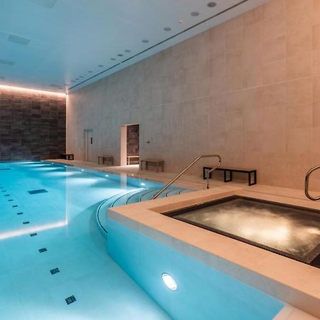 Citysuites 2 Aparthotel Манчестер Екстер'єр фото The photo shows an indoor swimming pool area. The pool is a bright blue color and features smooth, tiled surfaces. On one side, there is a hot tub area with steps leading into it. The walls are made of light-colored stone, and there is ambient lighti