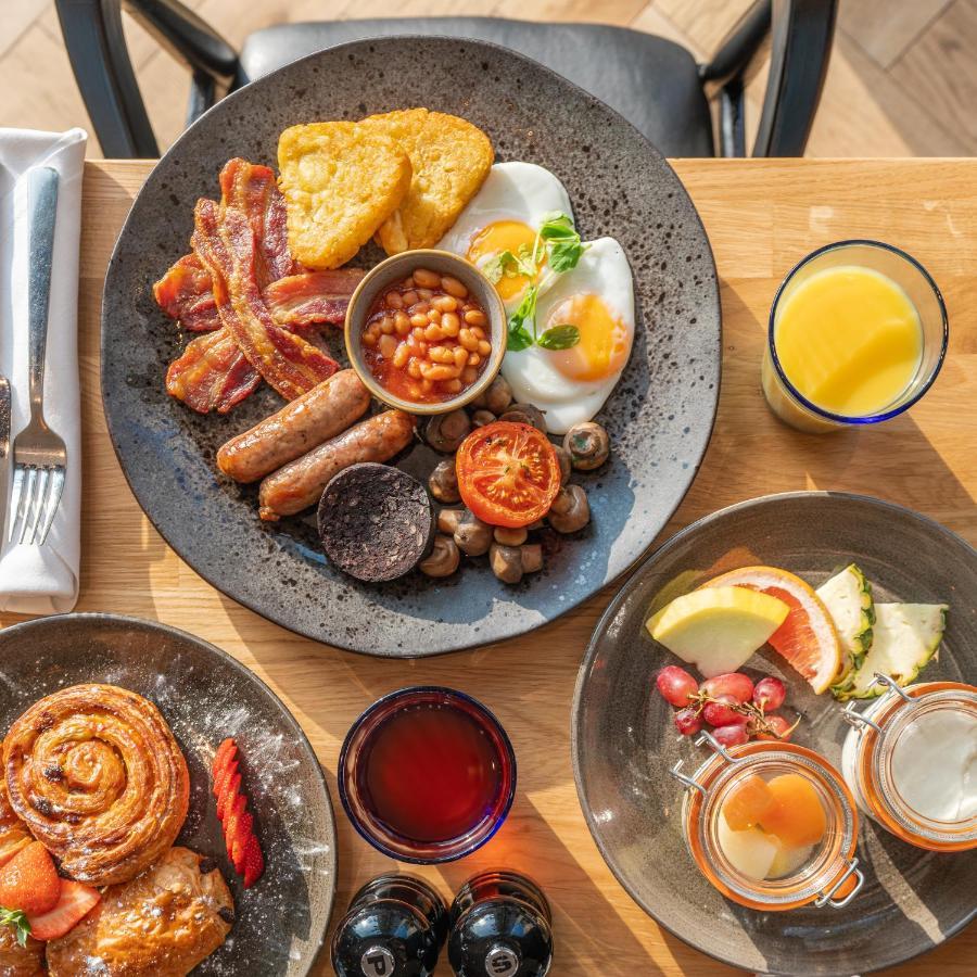 Citysuites 2 Aparthotel Манчестер Екстер'єр фото The photo showcases a delicious breakfast spread. On a large, dark plate, there are items including crispy bacon, two fried eggs, baked beans, a grilled tomato, sautéed mushrooms, sausage links, and slices of black pudding. There's also a few pieces 