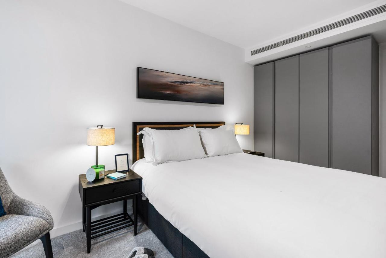 Citysuites 2 Aparthotel Селфорд Екстер'єр фото The photo shows a modern bedroom with a neatly made bed featuring white linens and pillows. Flanking the bed are two bedside tables, each with a lamp providing soft lighting. There is a piece of artwork above the bed, which appears to depict a landsc
