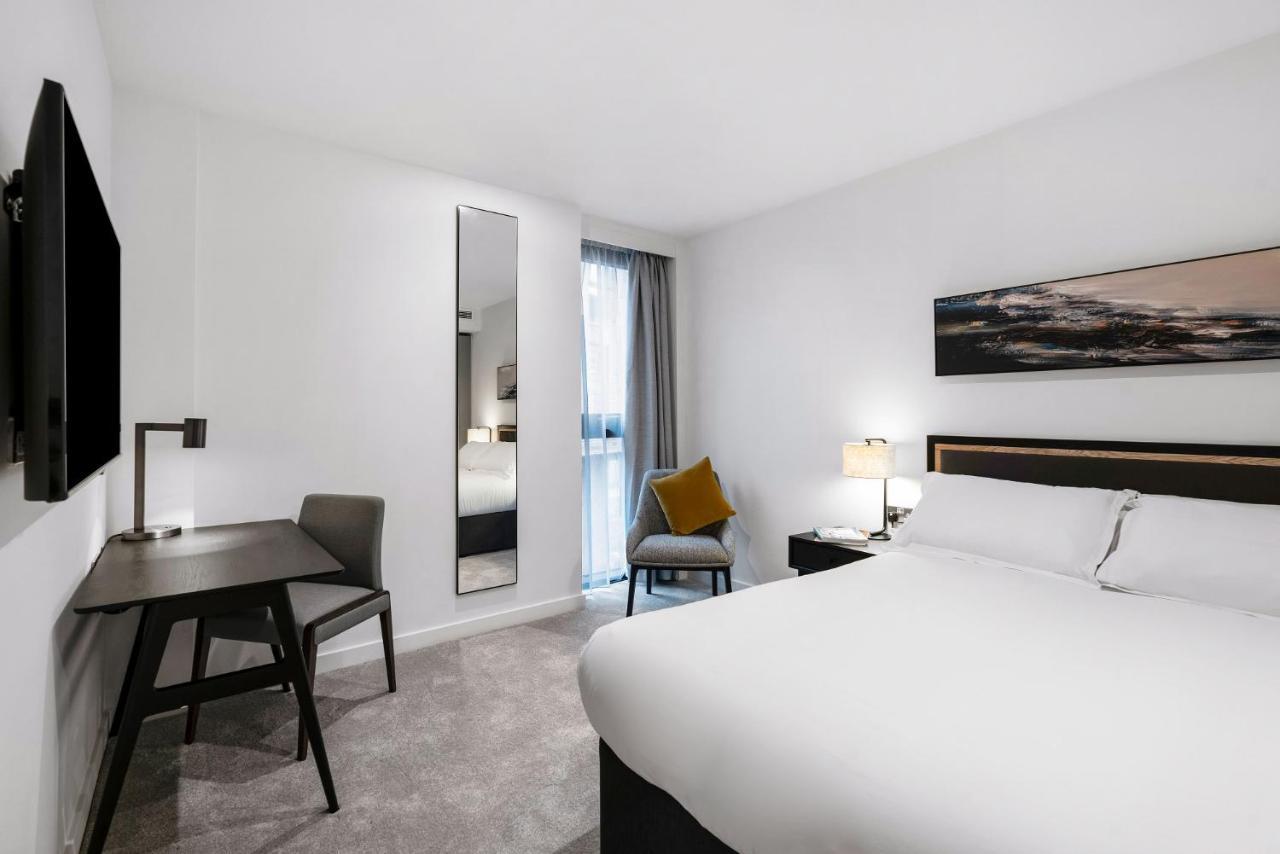Citysuites 2 Aparthotel Манчестер Екстер'єр фото The photo shows a modern hotel room with a clean and minimalist design. It features a large bed with white linens, a small desk with a chair, and a mirror mounted on the wall. There is a chair in one corner with a decorative pillow, and the room has 