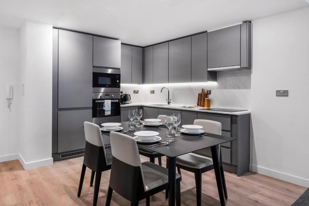 Citysuites 2 Aparthotel Селфорд Екстер'єр фото The photo shows a modern kitchen and dining area. The kitchen features sleek, gray cabinetry and a countertop that complements the overall aesthetic. There are built-in appliances, including an oven and refrigerator, arranged neatly. Next to the kitc