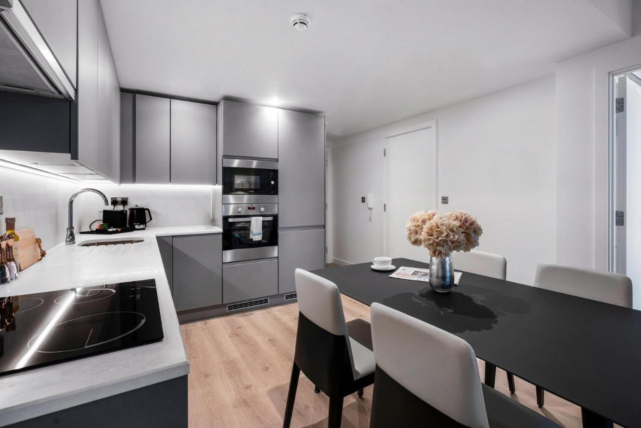 Citysuites 2 Aparthotel Манчестер Екстер'єр фото The photo shows a modern kitchen and dining area. The kitchen features sleek gray cabinets, a countertop with an embedded cooktop, and built-in appliances, including an oven and microwave. There’s a small coffee maker on the counter. Adjacent to the 