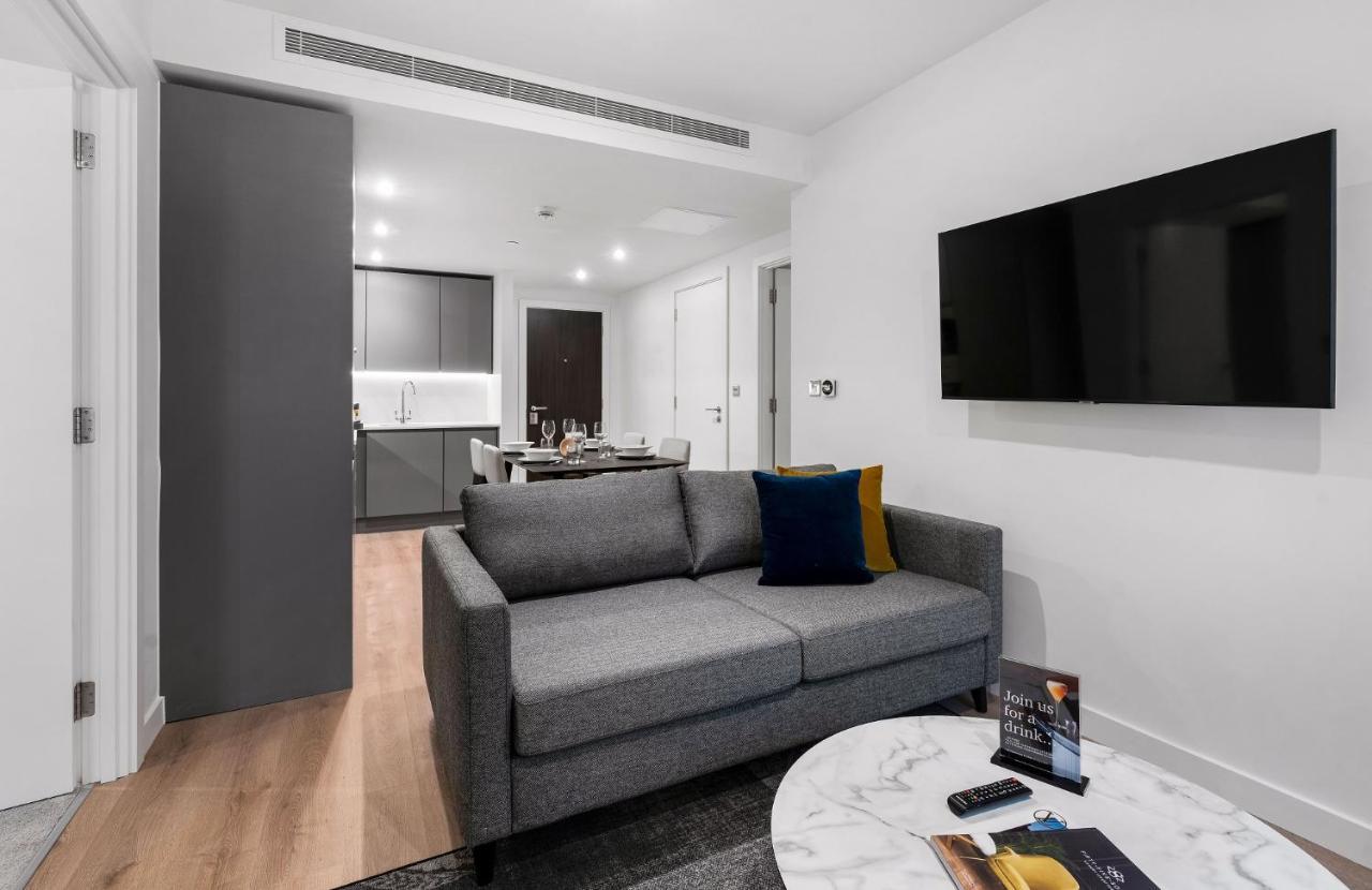 Citysuites 2 Aparthotel Селфорд Екстер'єр фото The photo shows a modern living space that includes a gray sofa with colorful cushions, a round marble coffee table, and a flat-screen TV mounted on the wall. In the background, there is a kitchen area featuring sleek cabinets. The flooring is light 