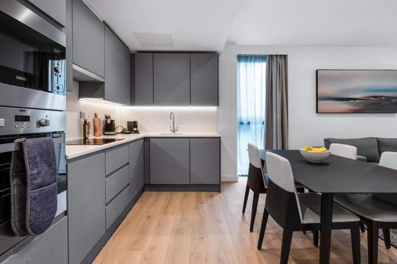 Citysuites 2 Aparthotel Селфорд Екстер'єр фото The photo shows a modern kitchen and dining area. The kitchen features sleek gray cabinetry, a white countertop, and built-in appliances such as an oven. There is a sink and some kitchen utensils displayed. The adjacent dining area contains a black t