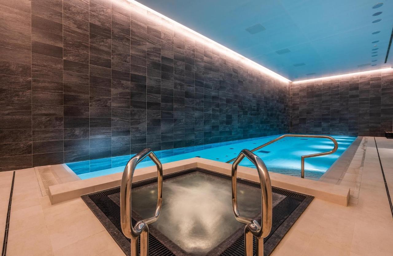 Citysuites 2 Aparthotel Манчестер Екстер'єр фото The photo shows a modern indoor swimming pool area. The pool features a sleek, rectangular design with a beautiful blue water that seems illuminated. Surrounding the pool are dark, textured walls, adding to the elegant atmosphere. There are dual meta