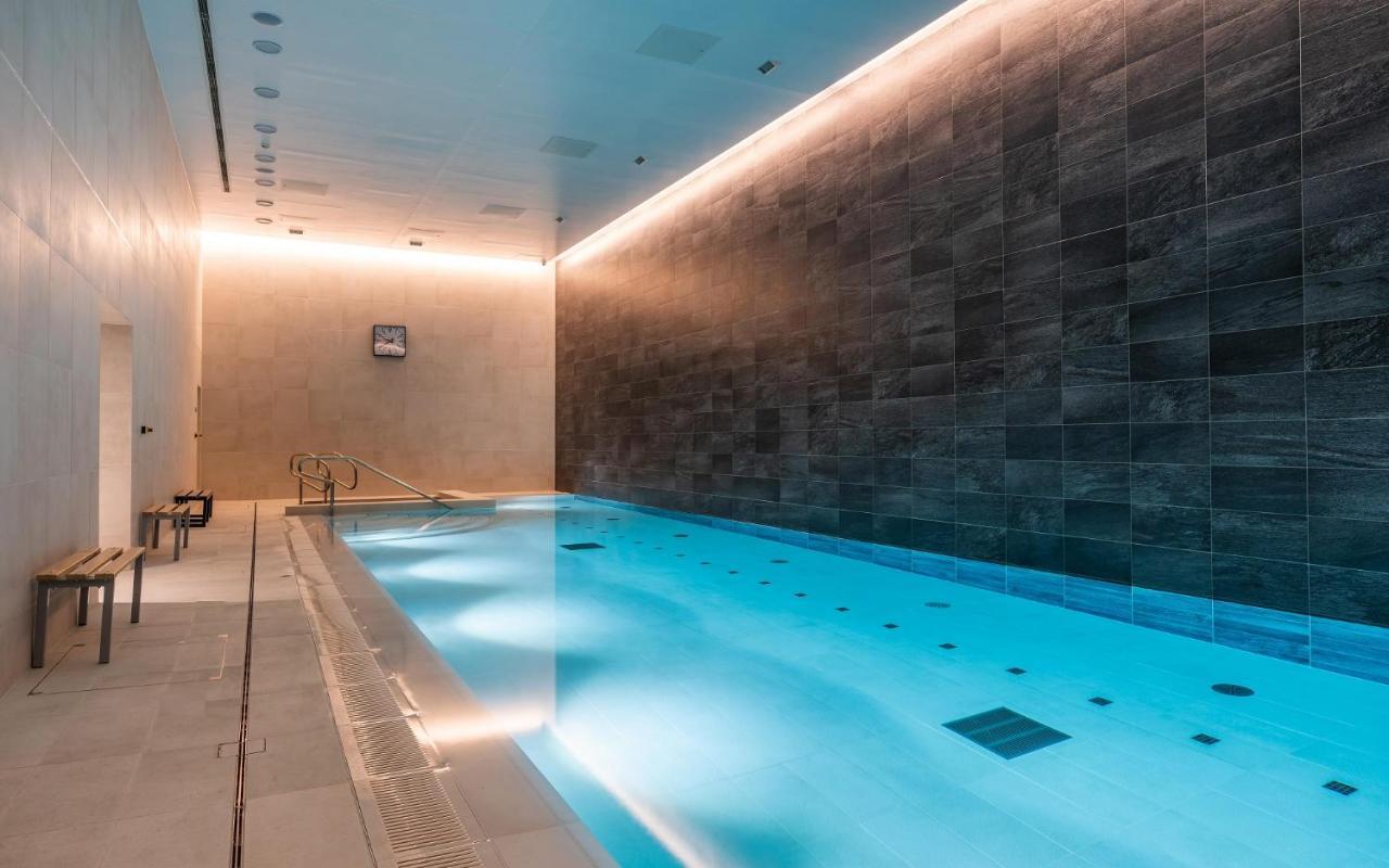 Citysuites 2 Aparthotel Манчестер Екстер'єр фото The photo shows an indoor swimming pool area. The pool is illuminated with a soft blue light, creating a calming atmosphere. The walls are designed with dark tiles, and there is a lighter tiled area surrounding the pool. Ambient lighting is installed