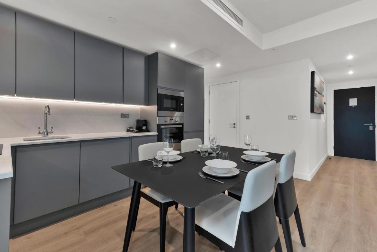 Citysuites 2 Aparthotel Селфорд Екстер'єр фото The photo shows a modern kitchen and dining area. There are sleek gray cabinetry and countertops, with a built-in oven and microwave. The kitchen is well-lit, featuring under-cabinet lighting that adds to the contemporary feel. In the dining area, th