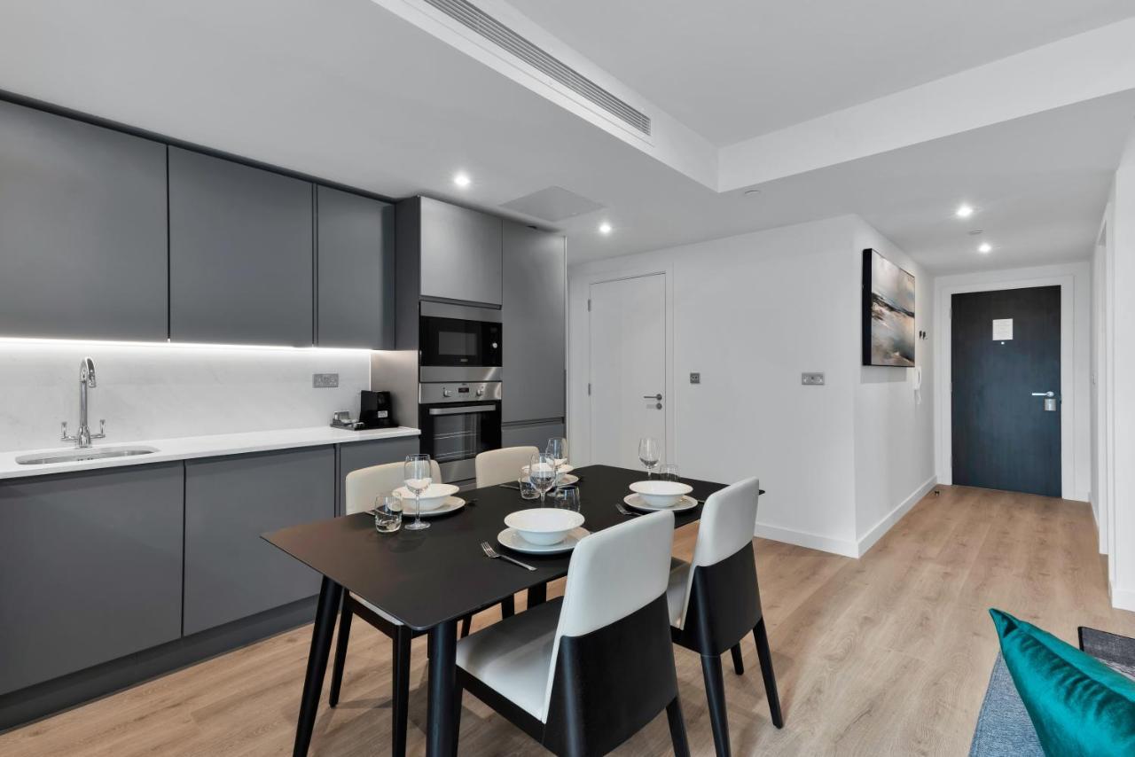 Citysuites 2 Aparthotel Селфорд Екстер'єр фото The image shows a modern kitchen and dining area. The kitchen features sleek gray cabinets with a white countertop, and it is equipped with appliances such as a microwave. There’s a dining table set for four, with white plates and glasses ready. The 