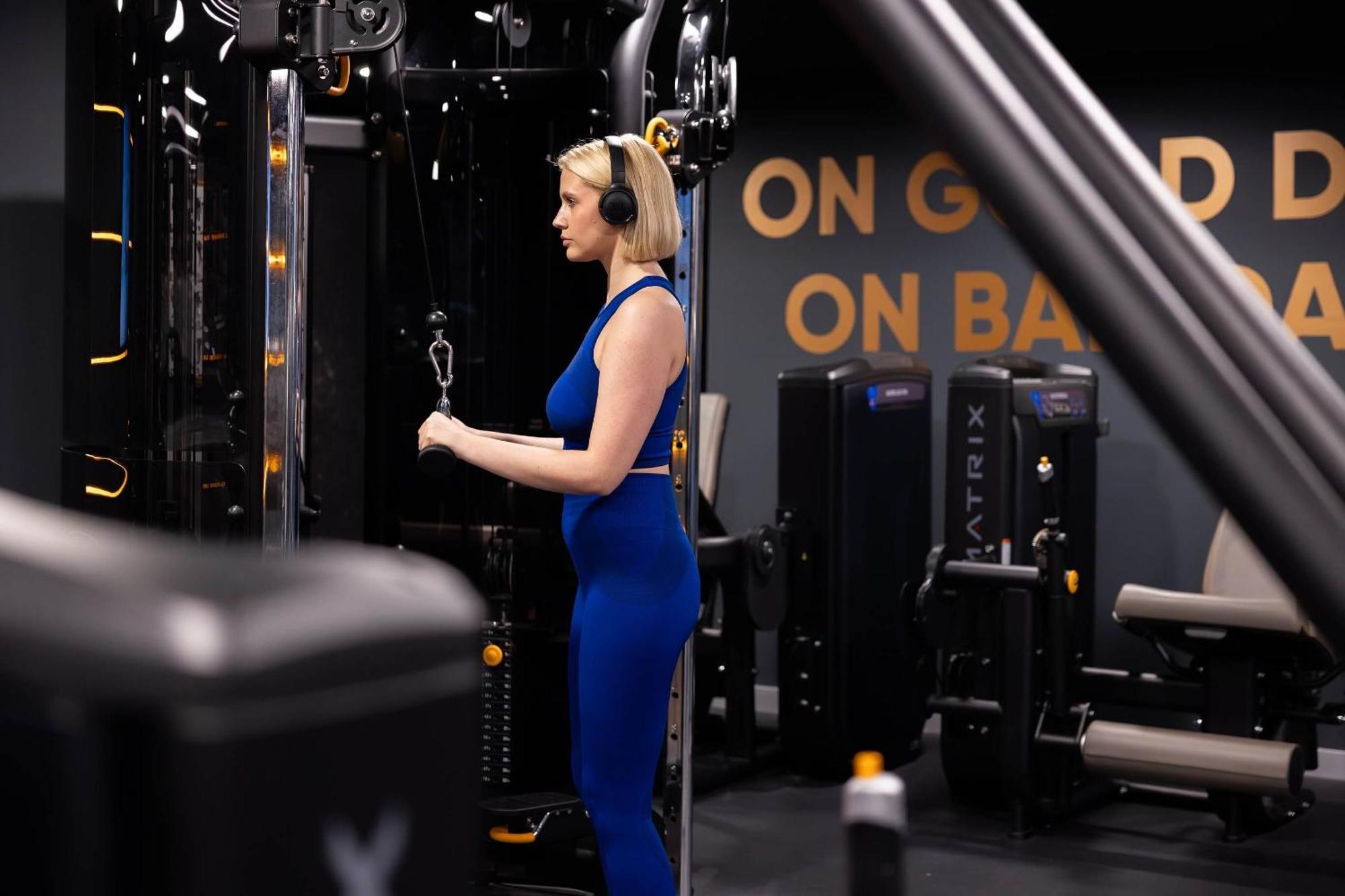 Citysuites 2 Aparthotel Манчестер Екстер'єр фото The photo shows a woman working out in a gym. She is wearing a blue athletic outfit and headphones while using a gym machine. The background features various other gym equipment and a wall with the words "ON GOOD ON BAD" displayed prominently. The se