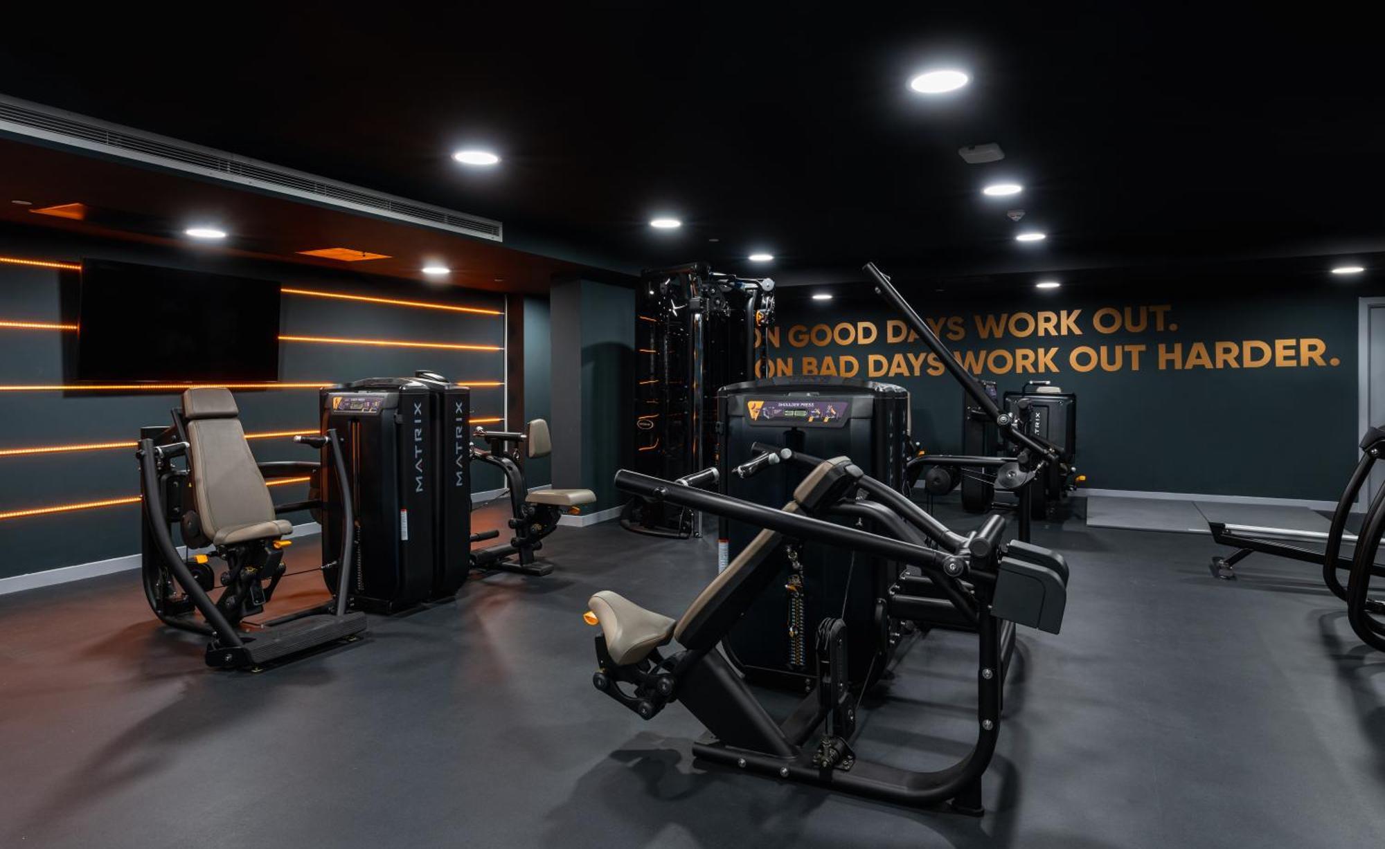 Citysuites 2 Aparthotel Манчестер Екстер'єр фото The photo shows a modern gym interior. The gym features various exercise machines, including weight training equipment. The flooring is dark, and the walls are adorned with motivational text that reads, "ON GOOD DAYS WORK OUT. ON BAD DAYS WORK OUT HA