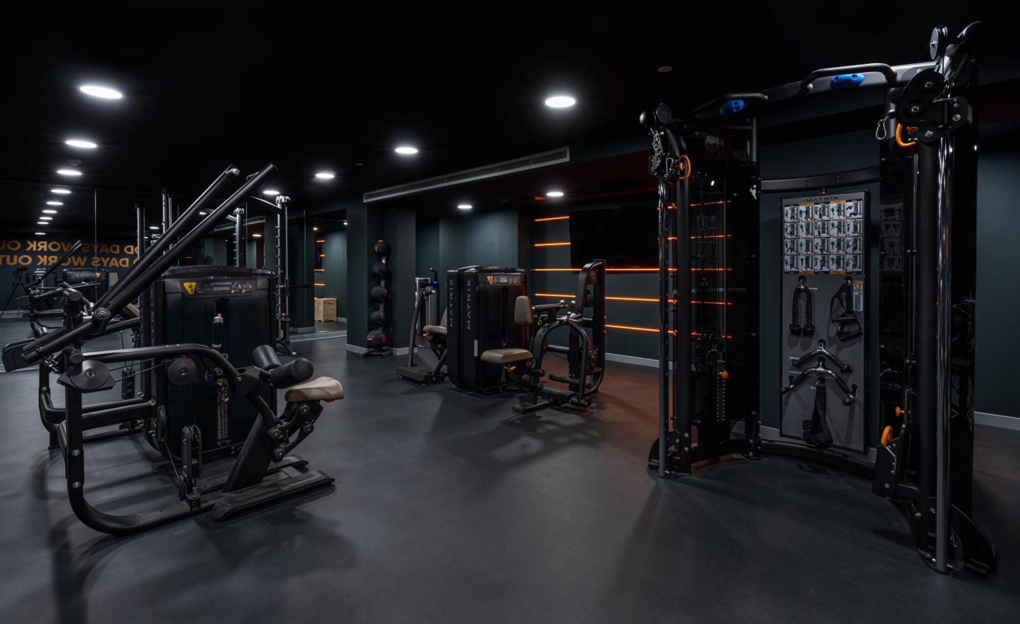 Citysuites 2 Aparthotel Манчестер Екстер'єр фото The photo shows a modern gym or fitness area with various workout machines. The space has a dark color scheme, featuring black walls and flooring. There are multiple pieces of exercise equipment, including stations for strength training, possibly tar