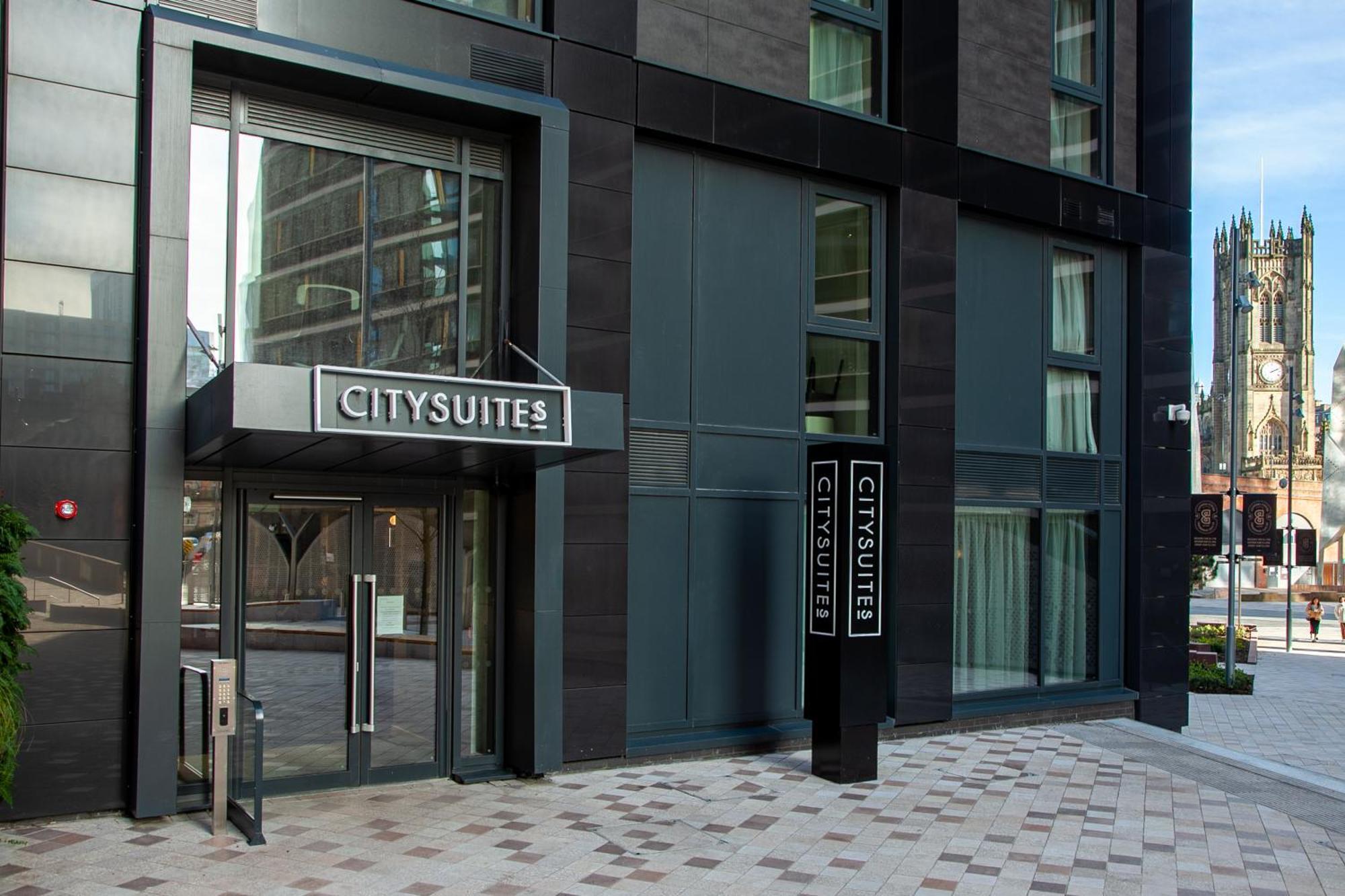 Citysuites 2 Aparthotel Манчестер Екстер'єр фото The photo shows the entrance to a modern building labeled "CITYSUITES." The entrance features large glass doors and a sleek, contemporary design. The building has dark exterior panels and large windows, suggesting a stylish and urban environment. The
