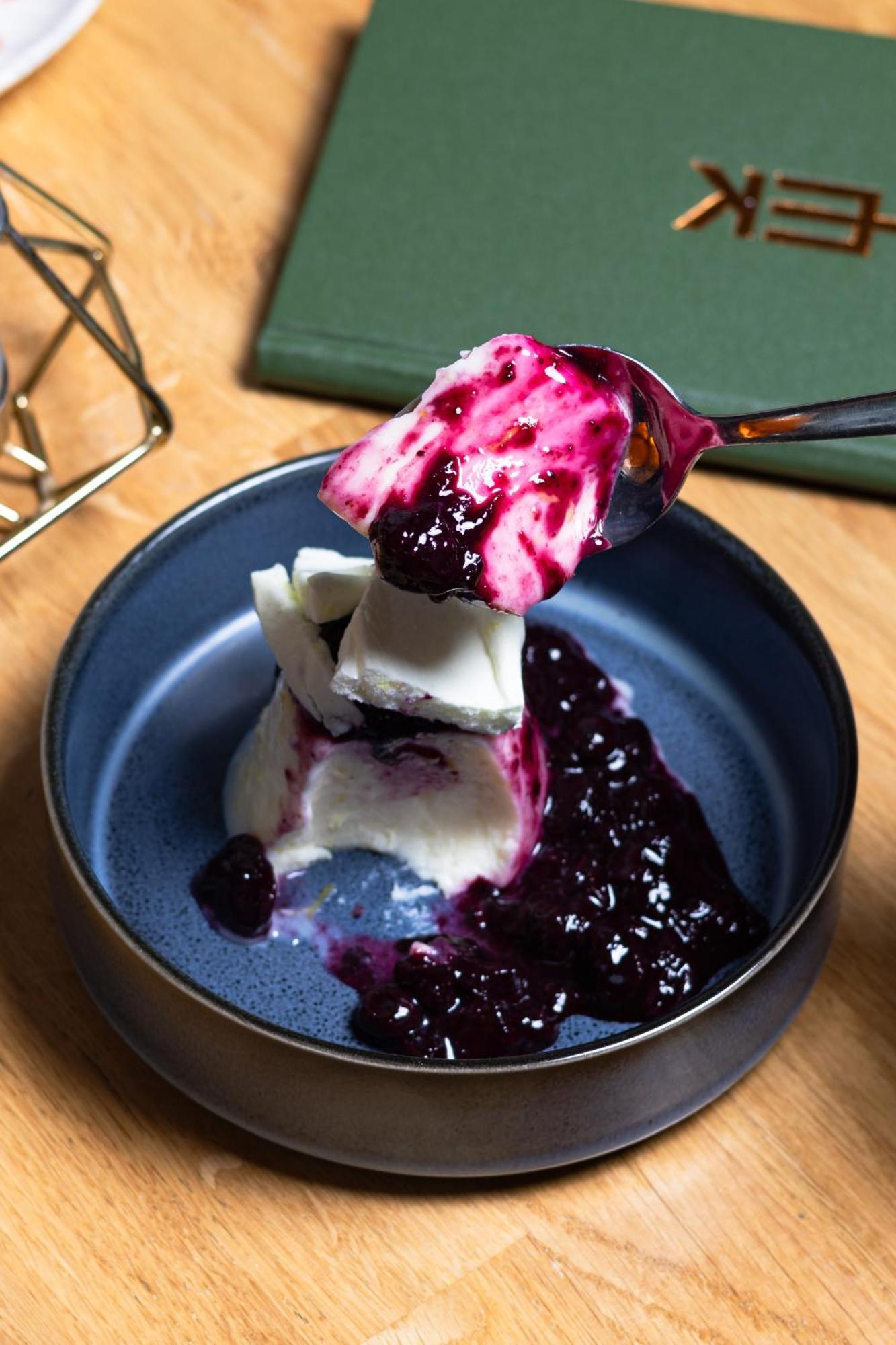 Citysuites 2 Aparthotel Селфорд Екстер'єр фото The photo shows a serving of dessert, likely a type of panna cotta or a creamy custard, partially dished out and accompanied by a rich berry sauce, possibly made from blueberries or blackberries. A spoon with some of the dessert and sauce is hovering